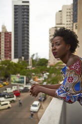 Woman wearing colorful dress standing on balcony looking out - VEGF02256