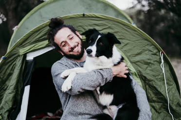 Glücklicher Mann, der seinen Hund in einem Zelt umarmt - EBBF00053