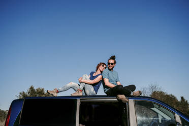 Happy couple sitting on the roof of a minivan - EBBF00058