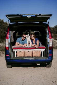 Porträt eines glücklichen Paares mit Hund im Kofferraum eines Minivans - EBBF00063