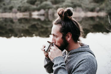 Man drinking from mug at lakeside - EBBF00071