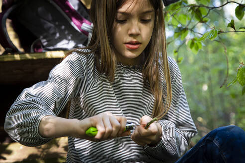 Mädchen schnitzt ein Stück Holz, das auf einem Hochsitz im Wald sitzt - LVF08886