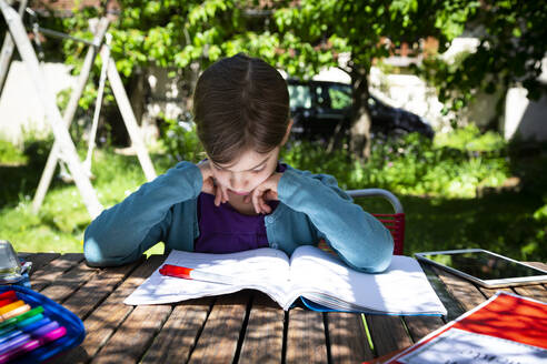 Girl sitting at garden table doing homework - LVF08890