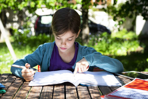 Girl sitting at garden table doing homework - LVF08891