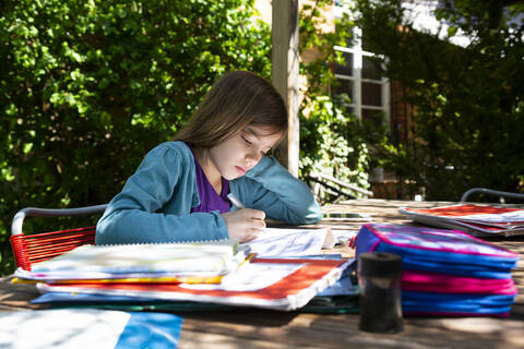Mädchen sitzt am Gartentisch und macht Hausaufgaben, lizenzfreies Stockfoto