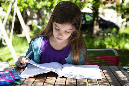 Girl sitting at garden table doing homework - LVF08893