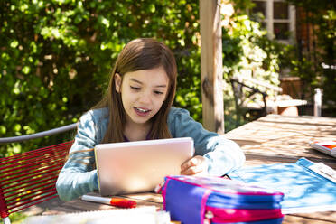 Mädchen sitzt am Gartentisch, macht Hausaufgaben und benutzt ein Tablet - LVF08894