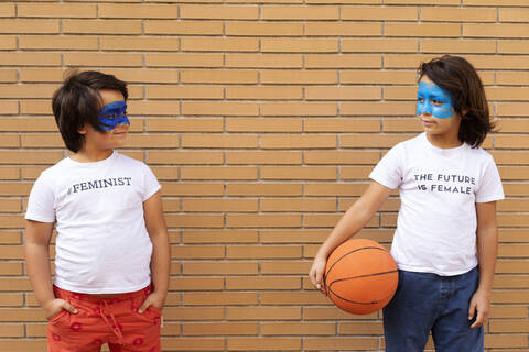 Porträt von zwei Brüdern mit aufgemalten blauen Masken im Gesicht, die T-Shirts mit feministischen Aufdrucken tragen, lizenzfreies Stockfoto