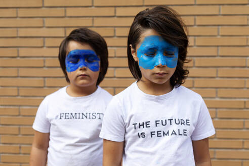 Porträt von zwei Brüdern mit aufgemalten blauen Masken im Gesicht, die T-Shirts mit feministischen Aufdrucken tragen - VABF02929