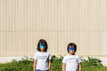 Zwei Brüder mit aufgemalten blauen Masken im Gesicht, die T-Shirts mit feministischen Aufdrucken tragen - VABF02938