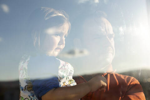 Porträt von Vater und kleiner Tochter hinter einer Fensterscheibe mit Blick in die Ferne, lizenzfreies Stockfoto