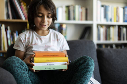 Junge sitzt zu Hause auf der Couch und hält einen Stapel von vier Büchern, lizenzfreies Stockfoto