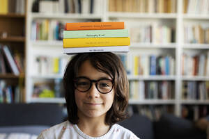 Porträt eines lächelnden Jungen, der einen Stapel Bücher auf seinem Kopf balanciert - VABF02952