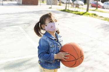 Portrait of little girl with basketball wearing protective mask - VABF02955