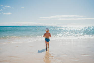 Junge, der an einem sonnigen Tag im Urlaub am Strand ins Wasser geht - CAVF80991