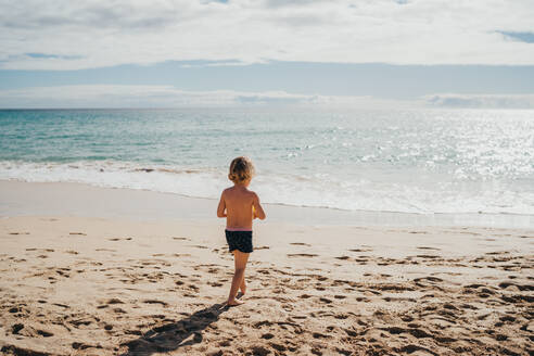 Junge, der an einem sonnigen Tag im Urlaub am Strand ins Wasser geht - CAVF80993