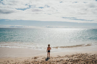 Junge, der an einem sonnigen Tag im Urlaub am Strand ins Wasser geht - CAVF80996