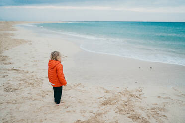 Ein Junge trägt an einem kalten Tag am Strand eine Jacke - CAVF80998