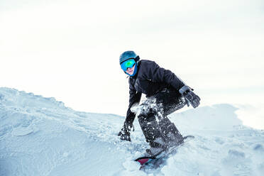A snowboarder crouched on a ridge of snow ready to push off - CUF55102