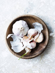 A wooden bowl with two garlic bulbs one whole and one split open. - CUF55109