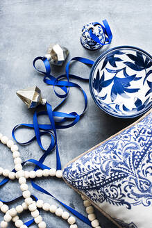 Draufsicht auf ein blaues und weißes Kissen und eine Schale mit blauem Band, weißen Perlen und silbernen Weihnachtskugeln. - CUF55128