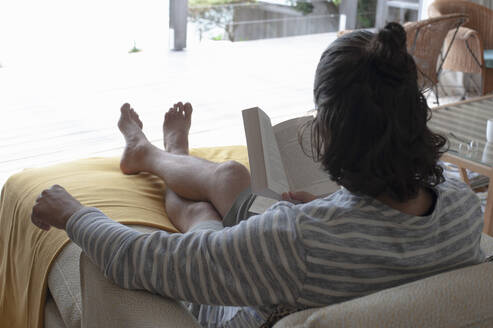 Rear view of a man sitting on a sofa reading a book. - CUF55139