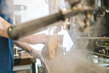 Nahaufnahme der Hände eines Barista, der an einer großen Kaffeemaschine einen Kaffee zubereitet, Dampf in der Luft. - CUF55166