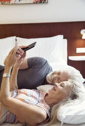 Ein Paar liegt auf einem Bett und schaut auf ein Mobiltelefon. - CUF55187
