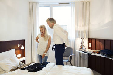 Ein Paar steht in einem Hotelzimmer und betrachtet die auf dem Bett ausgelegte Kleidung. - CUF55198