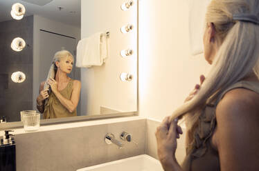 Eine Frau, die in einen Badezimmerspiegel schaut und ihren langen Pferdeschwanz glättet. - CUF55200