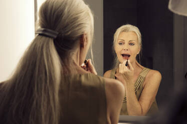 Rückansicht einer Frau, die in einen Spiegel schaut und Lippenstift aufträgt. - CUF55202