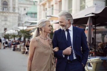 A couple walk arm in arm along a street with bars and market stalls in Vienna. - CUF55209