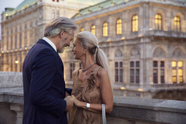 Ein Paar, das sich gegenübersteht und sich an den Händen hält, mit einem Wiener Gebäude im Hintergrund. - CUF55210