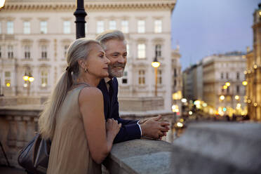 Ein Paar lehnt an einer Balustrade mit Blick auf Wien am Abend. - CUF55214