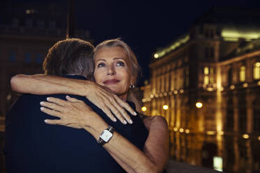 Eine Frau umarmt ihren Partner und lächelt ihm über die Schulter, während sie abends in Wien ausgeht. - CUF55217