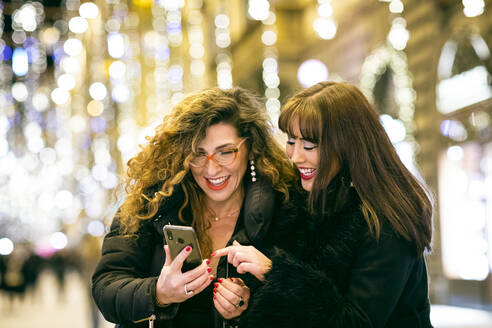 Zwei Frauen lächeln und schauen auf ein Handy in einer Straße in Florenz. - CUF55222