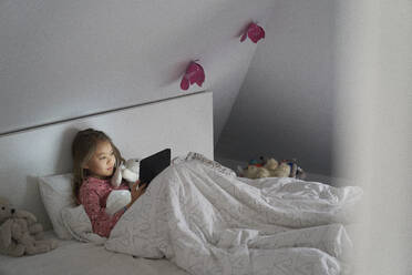 Home life, a school morning during lockdown. A girl lying in bed using a digital tablet. - CUF55233