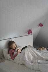 Home life, a school morning during lockdown. A girl lying in bed using a digital tablet. - CUF55234