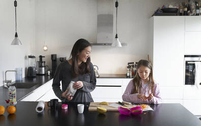 Home life, a school morning during lockdown. A girl and her mother in a kitchen cooking together - CUF55236