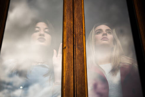 Two women standing next to each other looking out through a window. - CUF55241