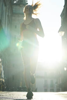 Eine junge Frau in Laufkleidung, die mit der Sonne im Rücken auf die Kamera zuläuft. - CUF55251