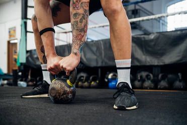 Tattooed arms and legs of a man holding a kettle bell on the floor. - CUF55263