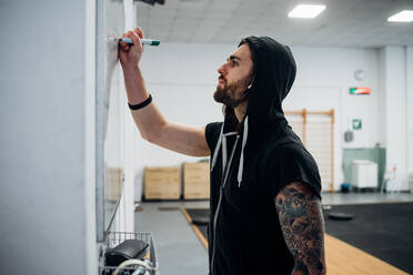 Man standing in a gym writing on a whiteboard. - CUF55264