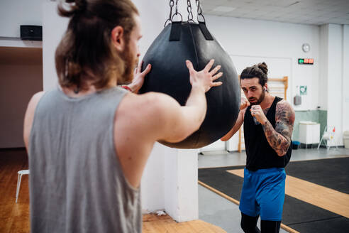 Rückansicht eines Mannes, der einen kleinen Boxsack für einen Boxer stabilisiert. - CUF55274