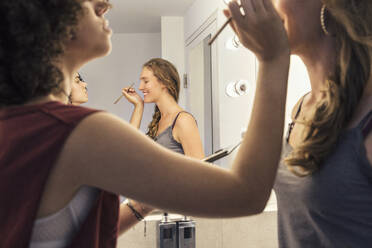 One woman putting make up on another woman with a reflection of them in the mirror. - CUF55282