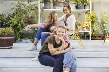 Vier lächelnde Frauen sitzen in einem Innenhof mit Pflanzen im Hintergrund. - CUF55287