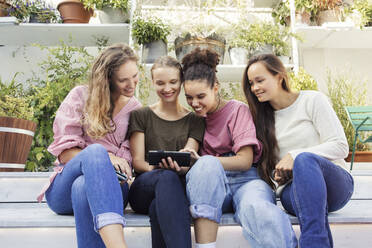 Four women sitting in a courtyard, looking at a phone and smiling. - CUF55288