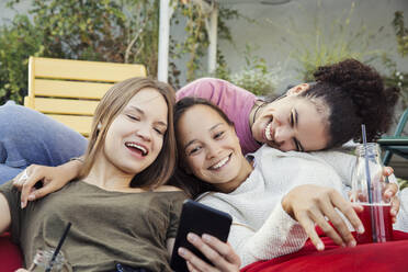 Drei Frauen lümmeln zusammen, lachen und schauen auf ein Handy. - CUF55293