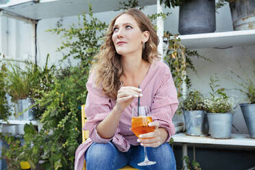Eine Frau sitzt auf einer Terrasse und trinkt etwas - CUF55295