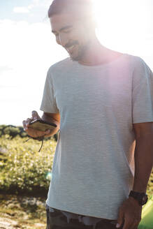Mann überprüft sein Smartphone an einem sonnigen Tag - CAVF81067